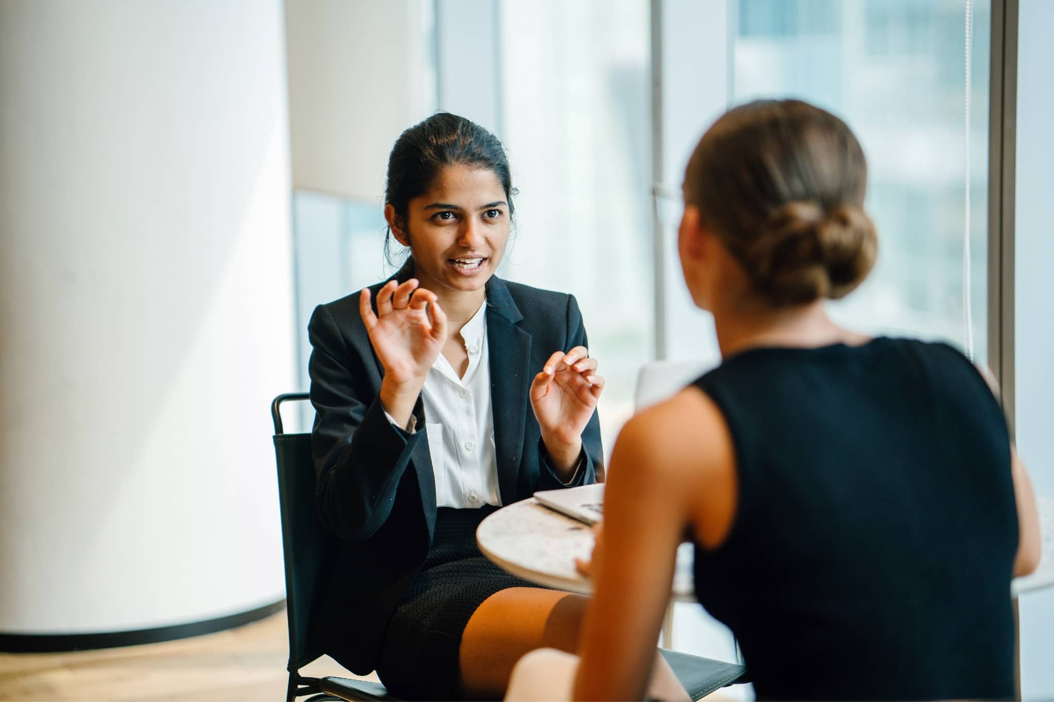 2 female workers discussing at a table - Pearson TalentLens
